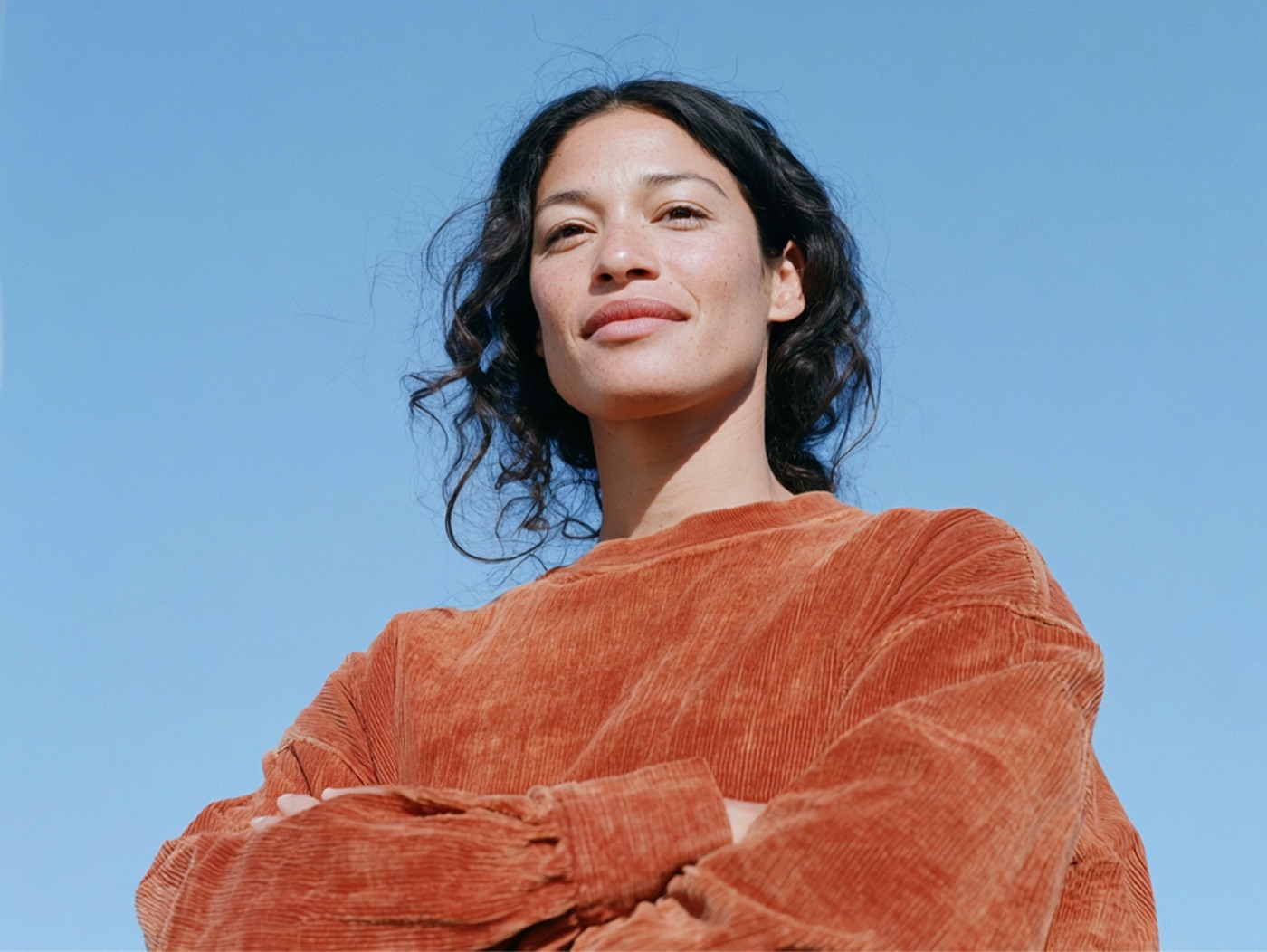 A woman with arms crossed standing against a clear blue sky